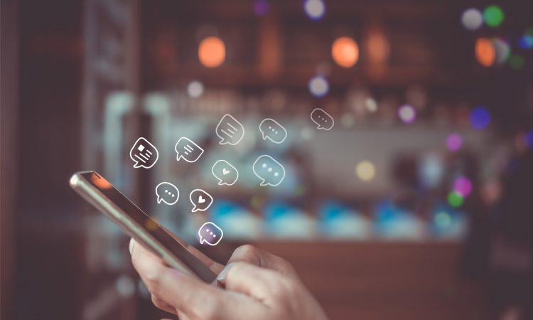 Hands typing on smartphone with chat bubbles above screen.