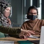 Man and woman wearing masks and looking at computer