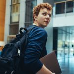 College student carrying his bag and laptop on campus.