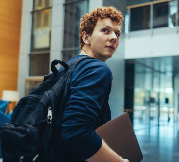 College student carrying his bag and laptop on campus.
