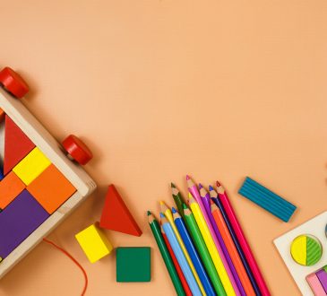 Colorful cubes, paints, pencils, blocks, modeling clay on orange background.