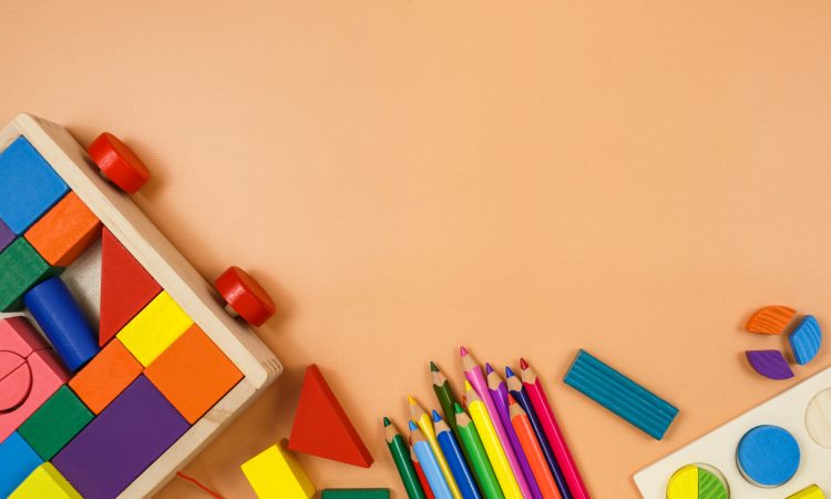 Colorful cubes, paints, pencils, blocks, modeling clay on orange background.