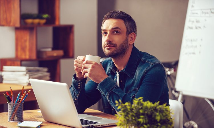 Man sitting at desk drinking coffee and daydreaming