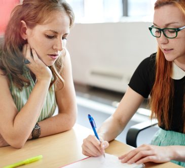 Two women meeting at table, with one writing while other looks on