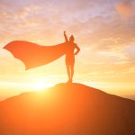 Silhouette of woman wearing cape on top of mountain during sunset