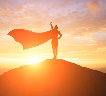 Silhouette of woman wearing cape on top of mountain during sunset