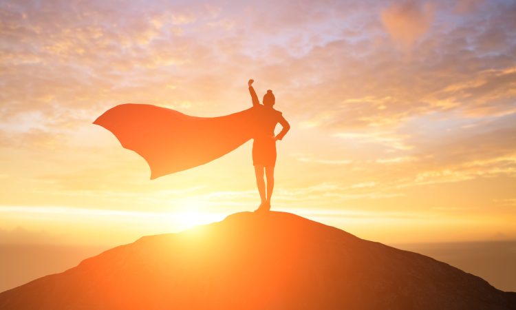 Silhouette of woman wearing cape on top of mountain during sunset