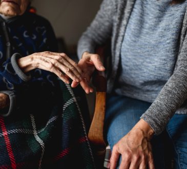 young person holding hands of old woman