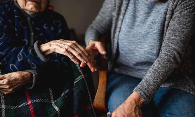young person holding hands of old woman