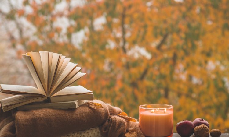 Autumn books scene - books in front of fall leaves, on top of blankets, beside candle