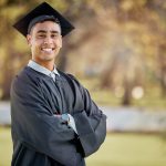 Young man posing for photo outdoors wearing graduation cap and gown