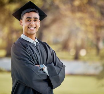 Young man posing for photo outdoors wearing graduation cap and gown