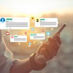 Hand holding phone with social media icons hovering above it