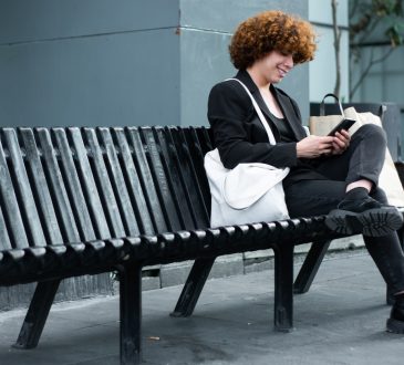 Non-binary person looking at phone on black bench outside of office