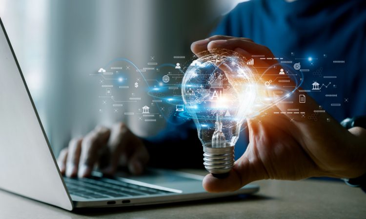 Person typing on laptop and holding glowing lightbulb in one hand with technology icons around it