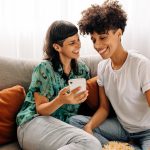 Lesbian couple laughing on couch together at home.