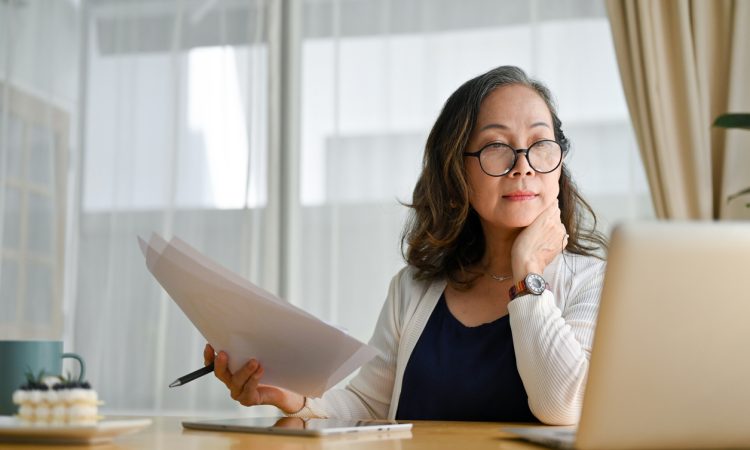 Older woman sitting at computer and examining paperwork