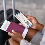 Close up hand of black businesswoman checking flight eticket on phone while holding passport and boarding pass.