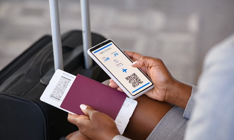 Close up hand of black businesswoman checking flight eticket on phone while holding passport and boarding pass.