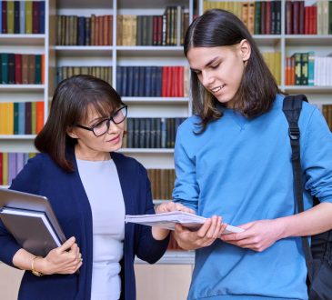 Teacher and student talking and looking at notebook in library.