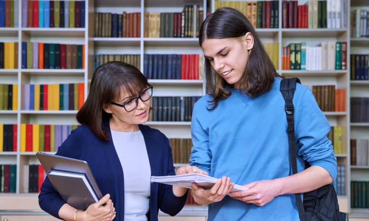 Teacher and student talking and looking at notebook in library.