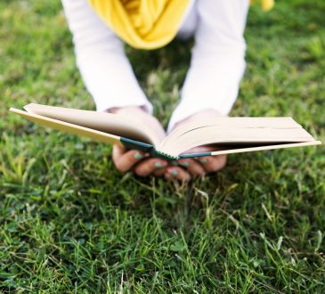 Person lying in grass reading book.