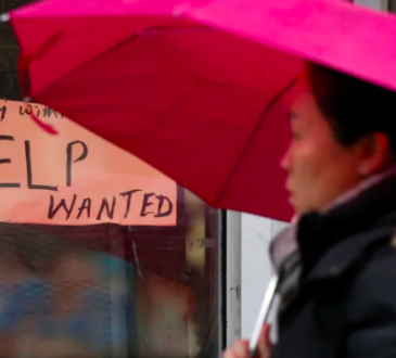 Woman with umbrella walking past store window with handwritten help wanted sign
