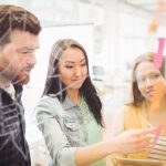 Three co-workers putting sticky notes on clear wall in office