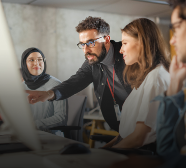A teacher helps three college-aged students who are working in a computer lab
