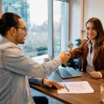 Man and woman shake hands across table during interview.