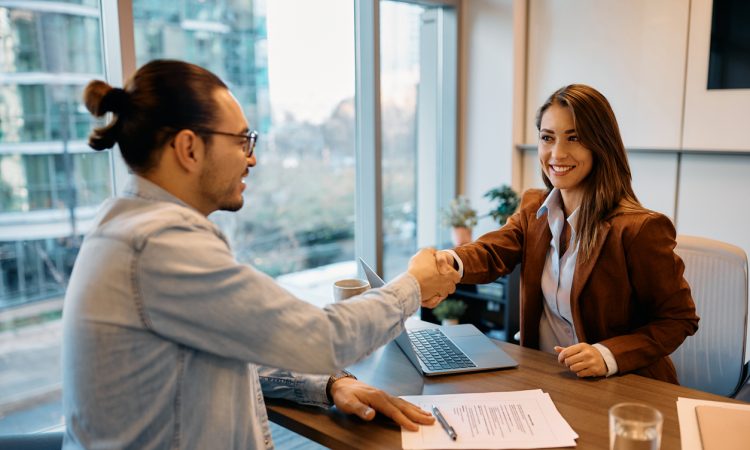 Man and woman shake hands across table during interview.