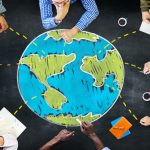 Photo illustration - bird's eye view of people sitting around globe drawn on table