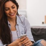 Woman sitting on couch, smiling and looking down at phone