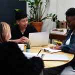 A group of co-workers of various genders having a meeting at a round table in an office.
