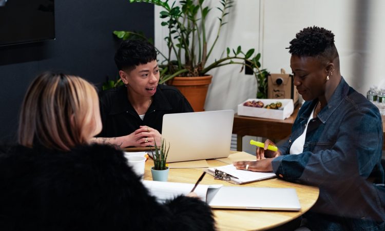 A group of co-workers of various genders having a meeting at a round table in an office.