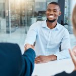 Two men shake hands across table during job interview.