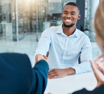 Two men shake hands across table during job interview.