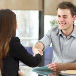 Man and woman shaking hands across desk.