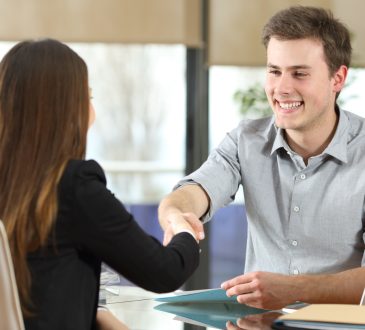 Man and woman shaking hands across desk.