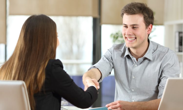 Man and woman shaking hands across desk.