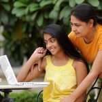 Mom looking over daughter's shoulder at laptop screen.