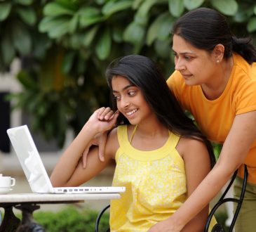 Mom looking over daughter's shoulder at laptop screen.