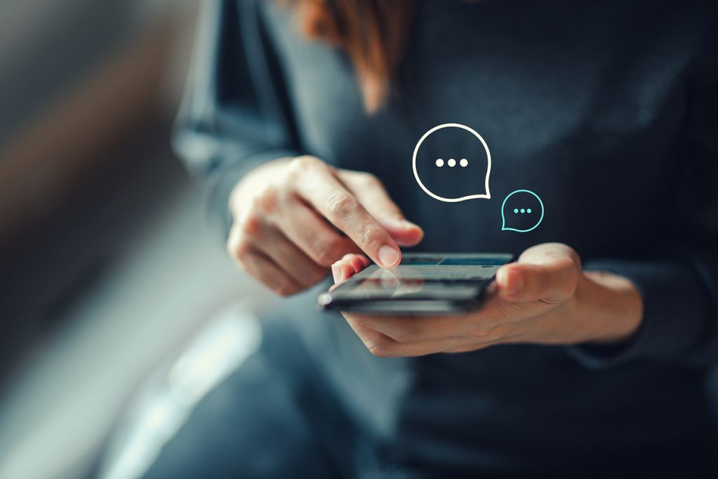 Women's hand typing on phone with chat bubbles