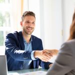 Smiling man shaking hands with interviewer across desk