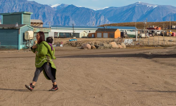 Inuit woman walking with baby in Pond Inlet, Baffin Island.