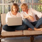 Two women working on laptop on outdoor patio furniture