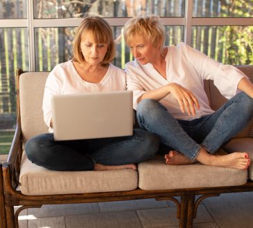 Two women working on laptop on outdoor patio furniture