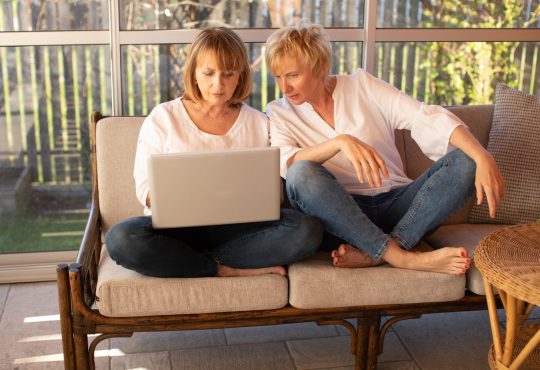Two women working on laptop on outdoor patio furniture