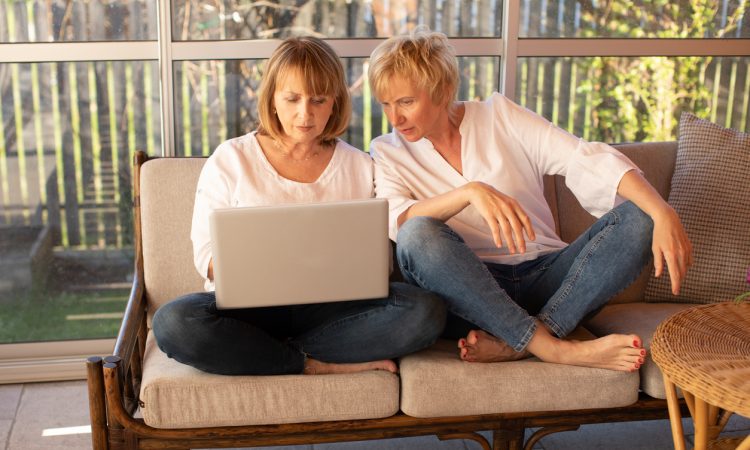 Two women working on laptop on outdoor patio furniture