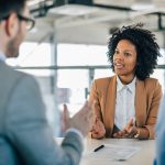 Black woman in job interview sitting across table from interviewers.